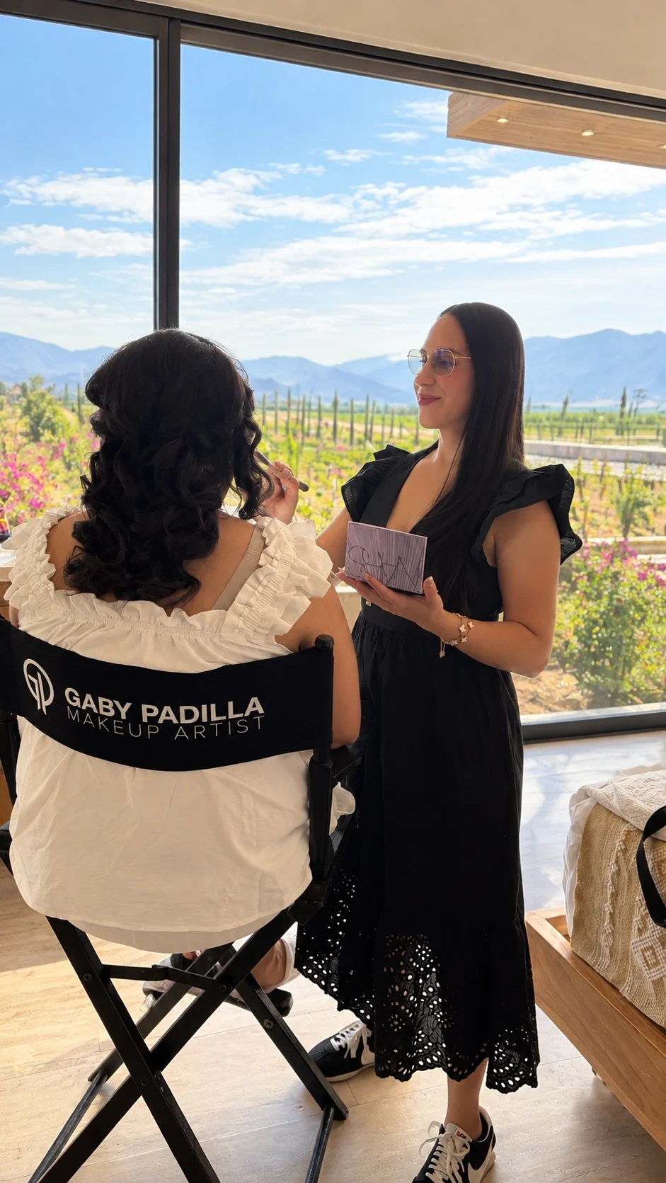 Gaby Padilla aplicando maquillaje profesional a una clienta con un paisaje de viñedos al fondo